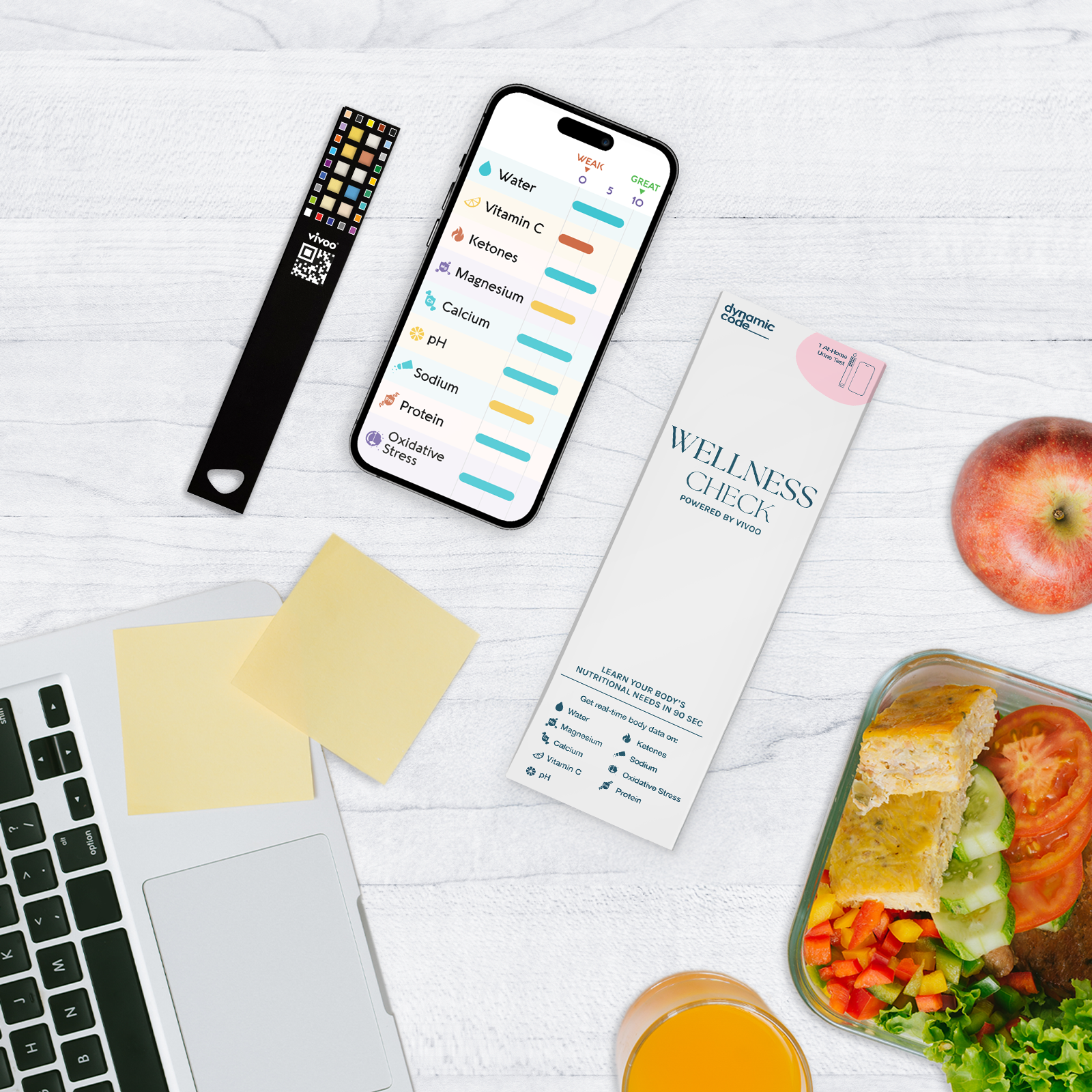 A wellness check kit displayed on a white surface, including a test strip, a smartphone showing wellness results (such as water, vitamin C, magnesium, and more), and a packaging labeled 'Wellness Check.' The setup also includes a laptop, sticky notes, a healthy meal with vegetables and bread, a glass of orange juice, and an apple, promoting a health-conscious lifestyle.